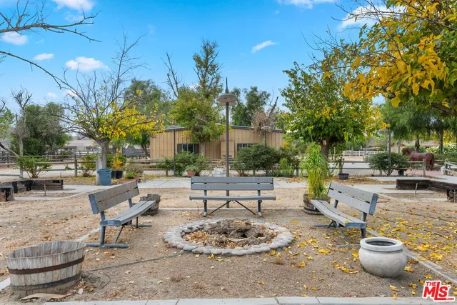 a view of a patio with a dining table and chairs and a fire pit with large trees