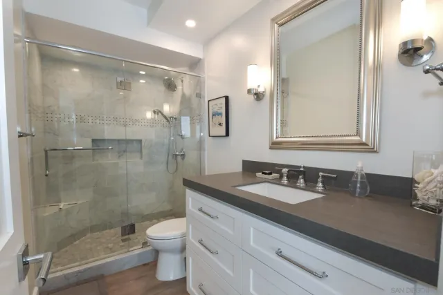 a bathroom with a granite countertop bathtub shower sink mirror and toilet