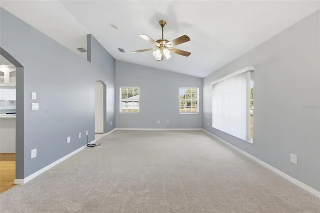an empty room with chandelier fan and windows