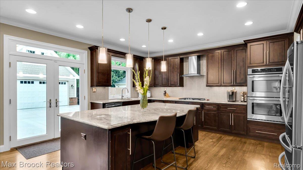 2253 Pembroke Road Birmingham, MI 48009 - Photo 12 of 56 Kitchen featuring wood-finish flooring, dark wood cabinetry, stainless steel appliances, a large center island with a light-toned countertop, and recessed lighting