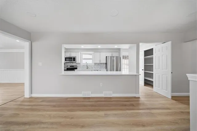a view of kitchen and empty room with wooden floor