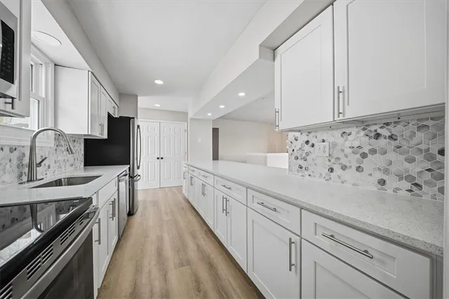 a large white kitchen with granite countertop a sink a stove a refrigerator and white cabinets