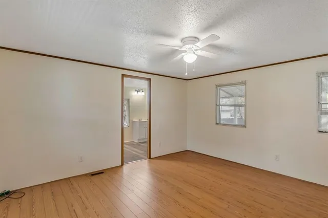 a view of an empty room with wooden floor and a ceiling fan