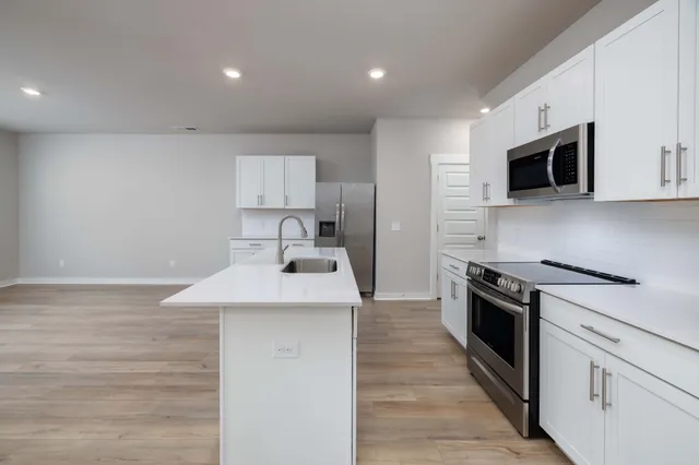 a kitchen with stainless steel appliances granite countertop a sink a stove top oven a refrigerator and white cabinets