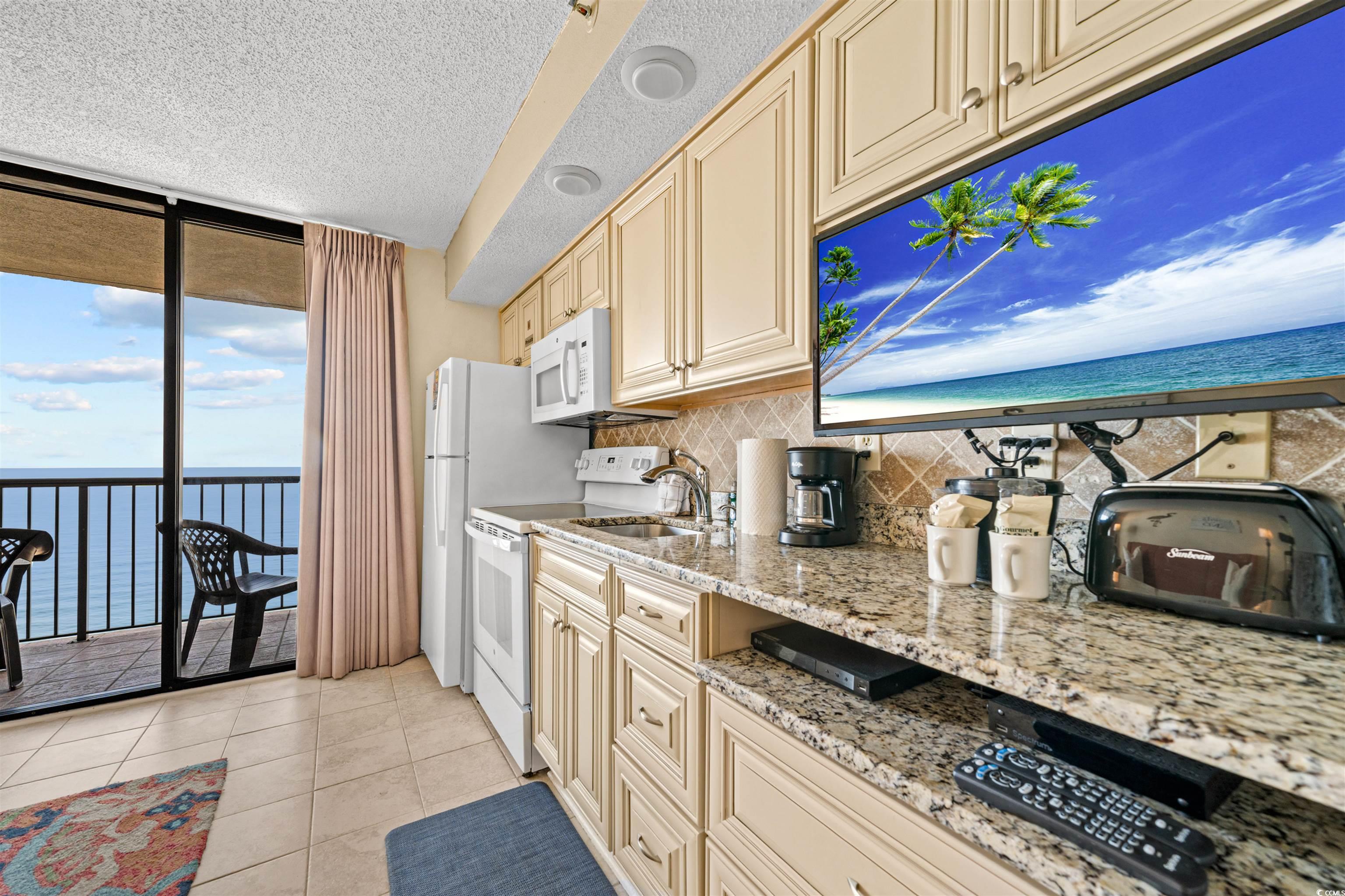 5308 North Ocean Boulevard, Unit 2006 Myrtle Beach, SC 29577 - Photo 10 of 37 Kitchen with floor to ceiling glass slider, cream cabinets, oceanfront view, white appliances, and granite countertops