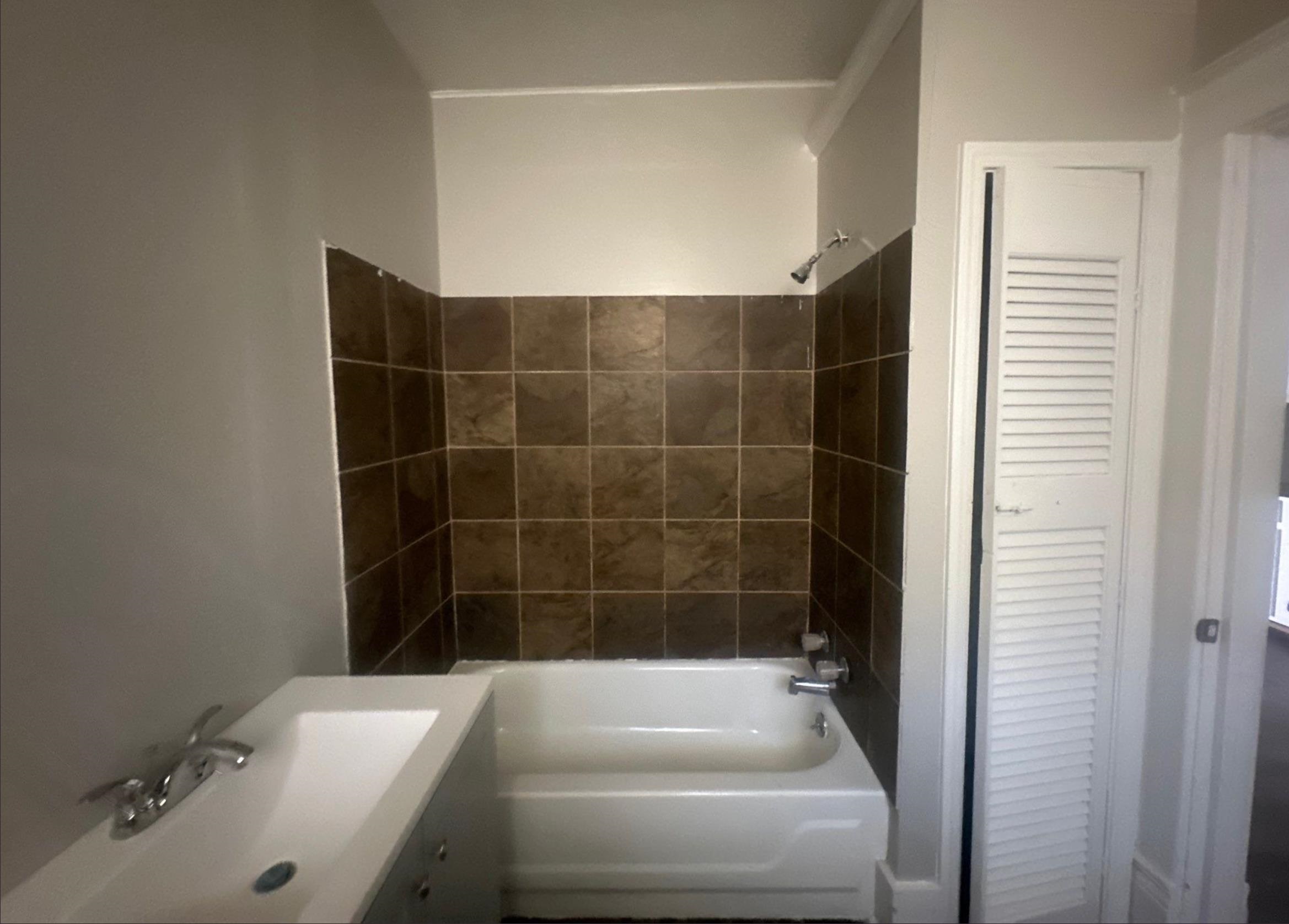 1165 Rayner Street Memphis, TN 38106 - Photo 11 of 16 Bathroom featuring a white bathtub, brown tiled shower surround, wall-mounted showerhead, and a white sink with chrome fixtures
