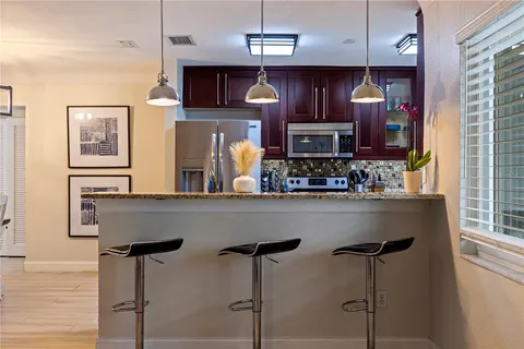 a kitchen with stainless steel appliances granite countertop a refrigerator a sink dishwasher a dining table and chairs with wooden floor