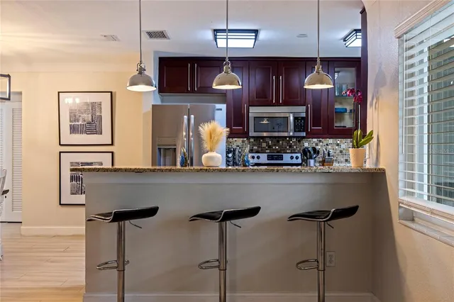 a kitchen with stainless steel appliances granite countertop a refrigerator a sink dishwasher a dining table and chairs with wooden floor