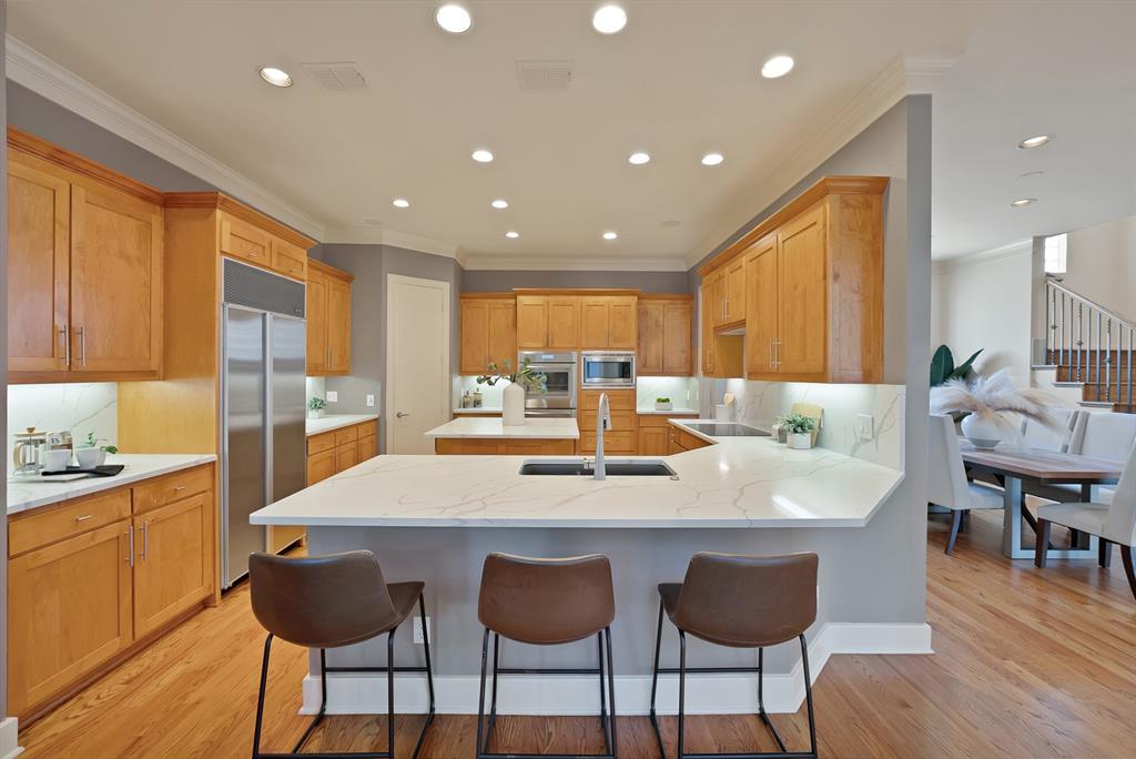 4010 Rawlins Street Dallas, TX 75219 - Photo 11 of 40 Kitchen featuring a peninsula, light wood finished floors, decorative backsplash, ornamental molding, and a breakfast bar area