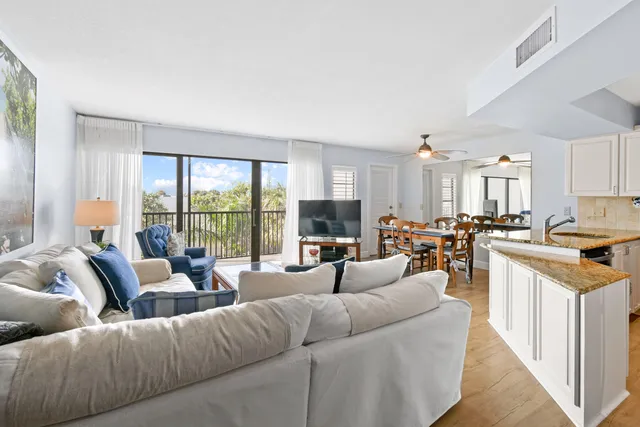 a living room with furniture large windows and a view of kitchen