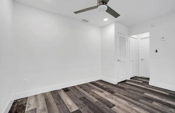 an empty room with wooden floor ceiling fan and window