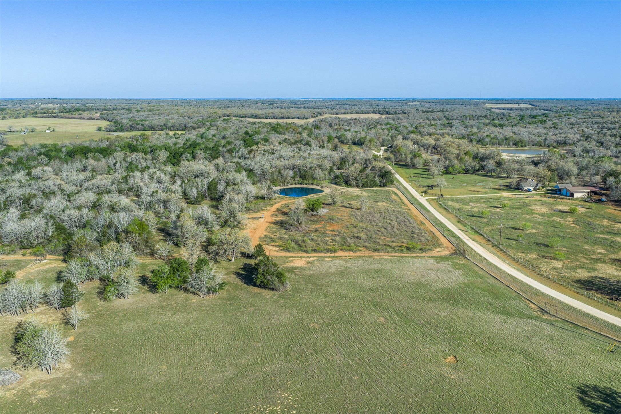 2313 Highway 79 Milano, TX 76556 - Photo 16 of 40 Expansive aerial landscape featuring a large grassy field, a circular pond, and a long unpaved road