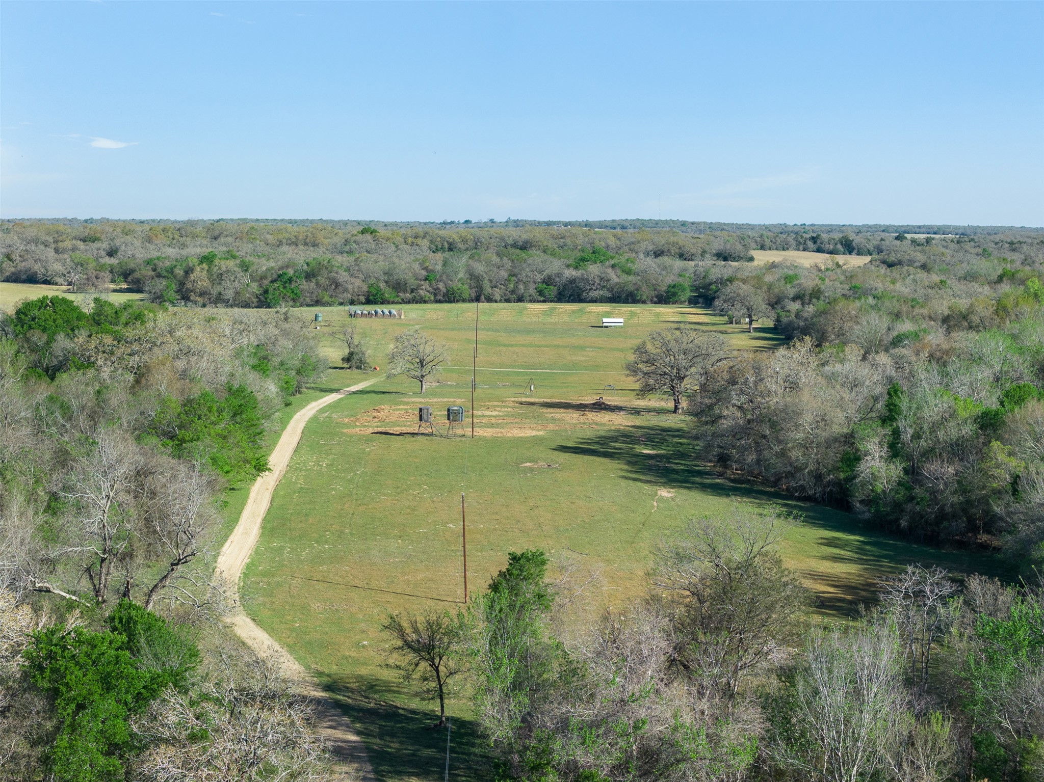 2313 Highway 79 Milano, TX 76556 - Photo 19 of 40 Expansive open field surrounded by mature trees, featuring a long unpaved path, two elevated structures, and a distant white shed