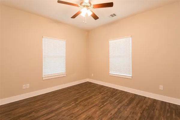 an empty room with wooden floor chandelier fan and windows