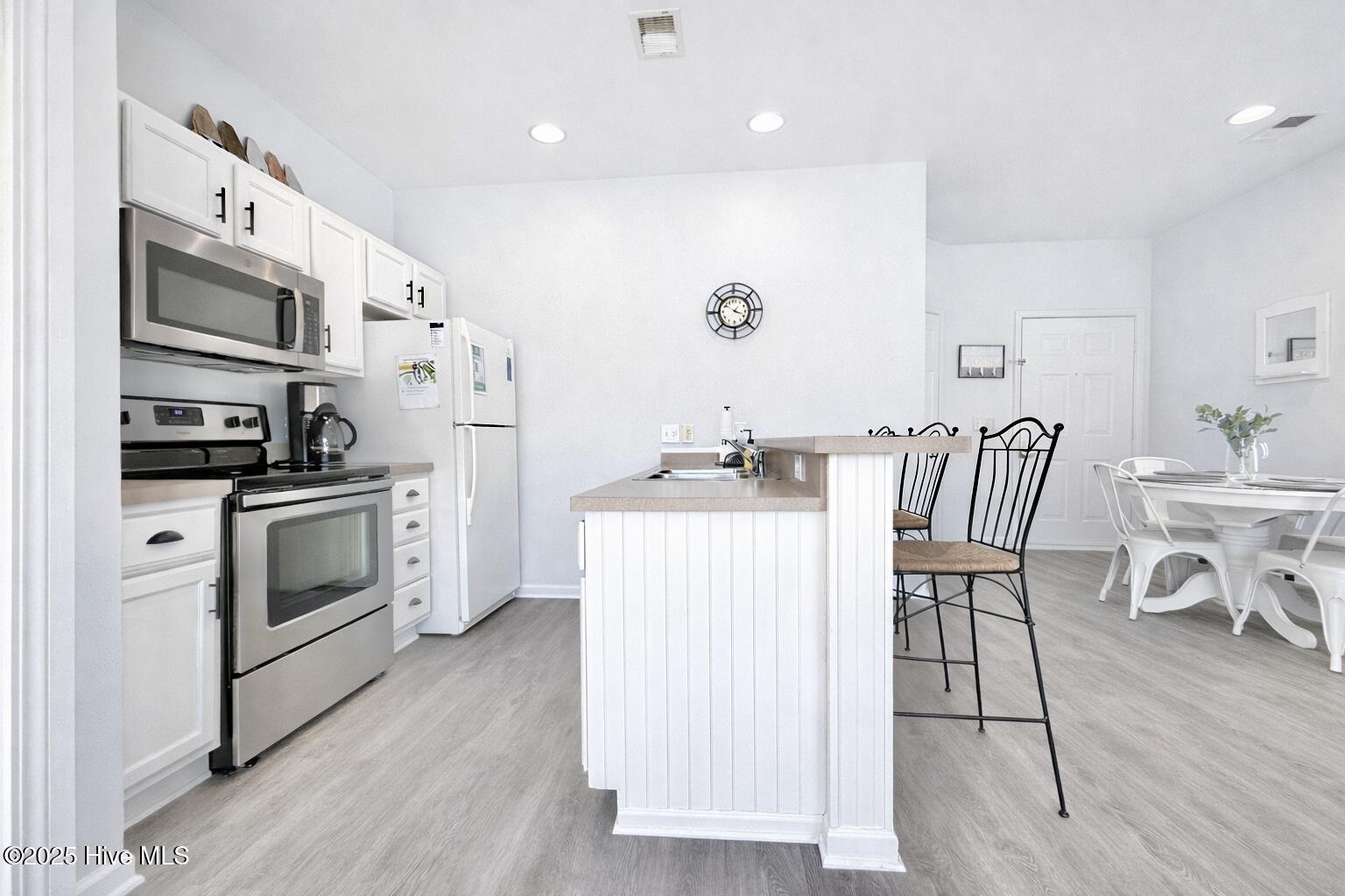 165 Royal Poste Road, Unit 2911 Sunset Beach, NC 28468 - Photo 5 of 24 Updated kitchen with white cabinetry, stainless steel appliances, breakfast bar, and open sightlines to living area.