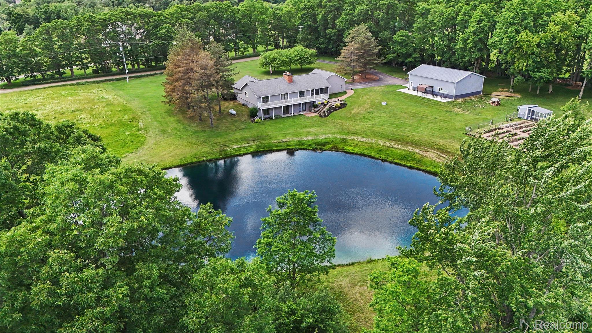5465 South Lake George Road Metamora, MI 48455 - Photo 50 of 61 Expansive grounds featuring a private pond, a two-story residence with a full-width upper balcony, a separate outbuilding, multiple garden beds, and surrounding mature trees