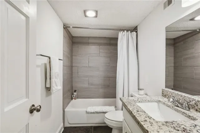 a bathroom with a granite countertop bathtub shower sink vanity and toilet