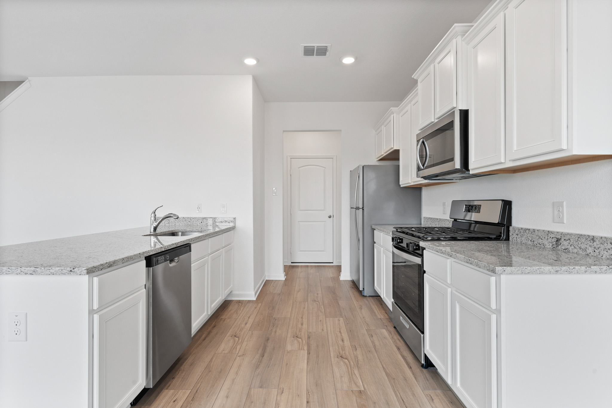 409 Silent Meadow Run Maxwell, TX 78656 - Photo 4 of 10 Kitchen with stainless steel appliances, white cabinetry, light stone countertops, light wood-type flooring, and a peninsula