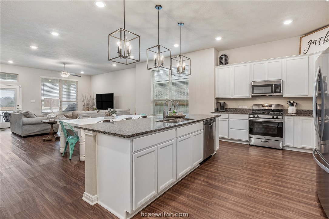 a kitchen with stainless steel appliances kitchen island granite countertop a sink a stove and a wooden floor