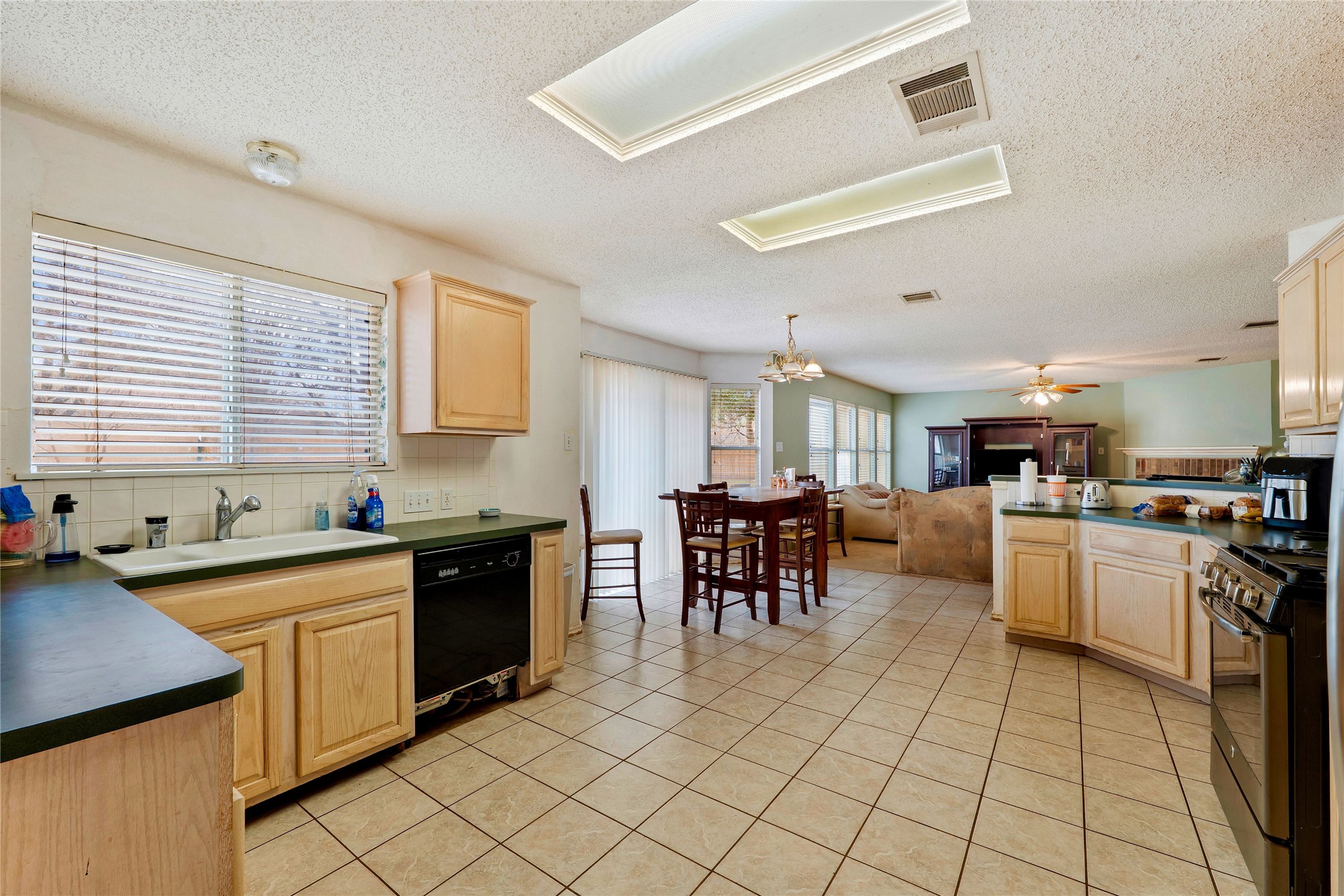 4008 Springwillow Lane Round Rock, TX 78681 - Photo 4 of 29 Kitchen with dark countertops, light wood finish cabinets, black appliances, decorative backsplash, light tile patterned flooring, and a textured ceiling