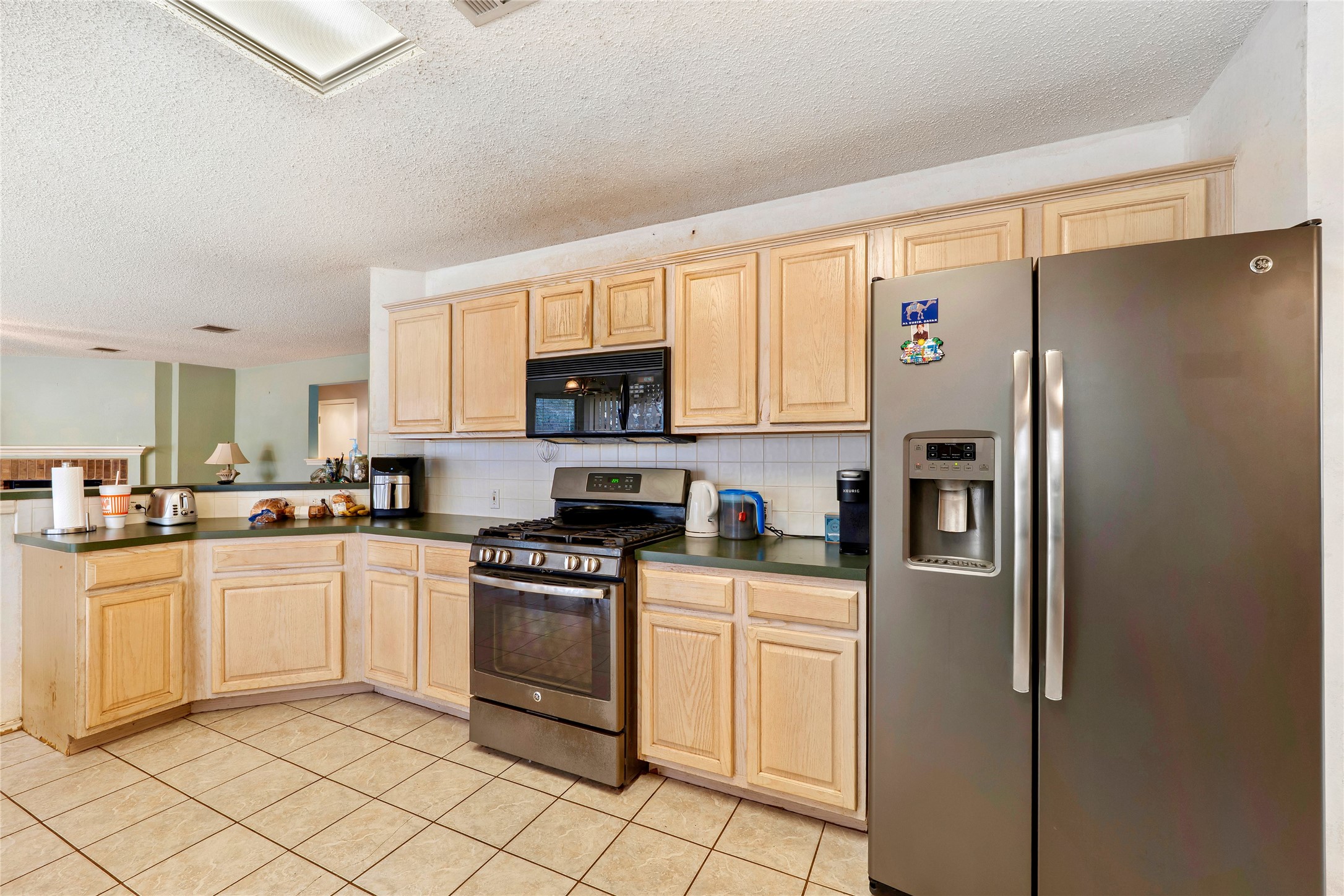 4008 Springwillow Lane Round Rock, TX 78681 - Photo 5 of 29 Kitchen featuring stainless steel appliances, light wood finish cabinets, dark countertops, a textured ceiling, light tile patterned flooring and backsplash