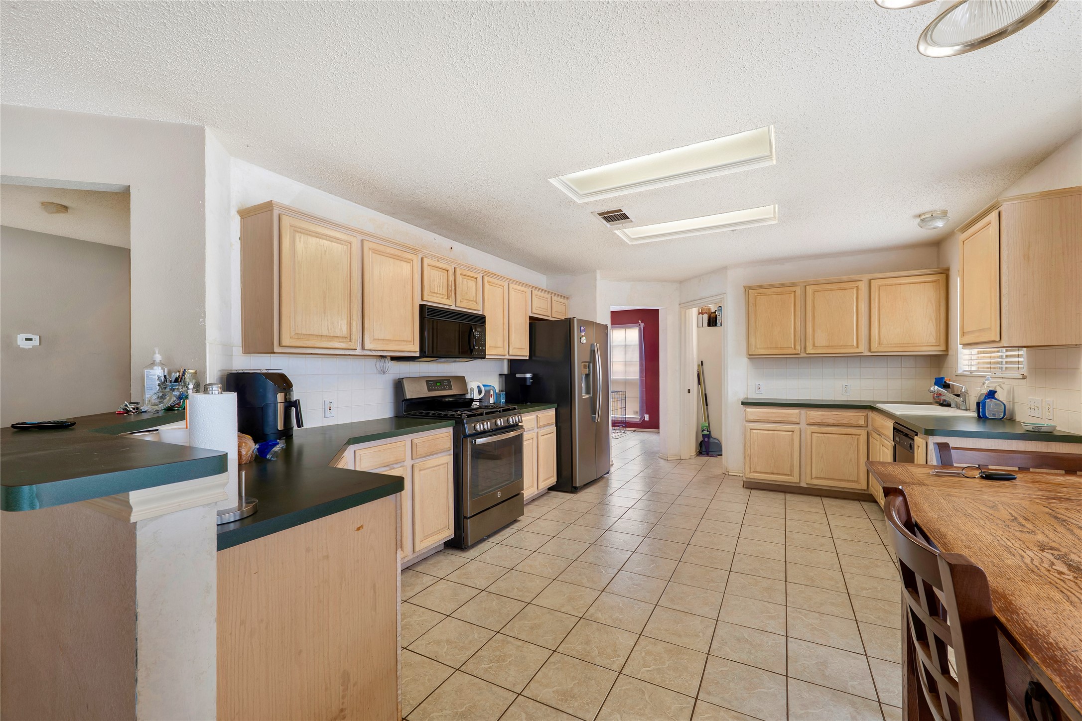 4008 Springwillow Lane Round Rock, TX 78681 - Photo 6 of 29 Kitchen featuring light wood finish cabinets, stainless steel appliances, a textured ceiling, light tile patterned flooring, and decorative backsplash
