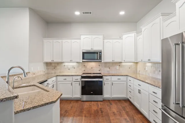 a kitchen with white cabinets appliances a sink and a window