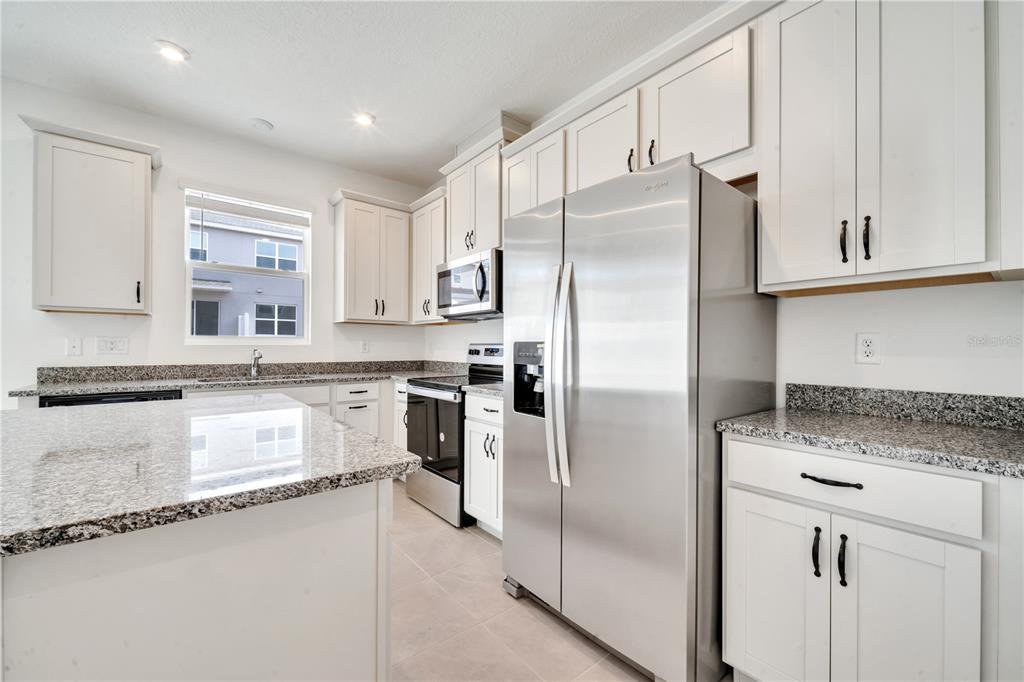 9068 Ocean Tide Way Kissimmee, FL 34747 - Photo 11 of 42 a kitchen with stainless steel appliances granite countertop a refrigerator a sink and white cabinets