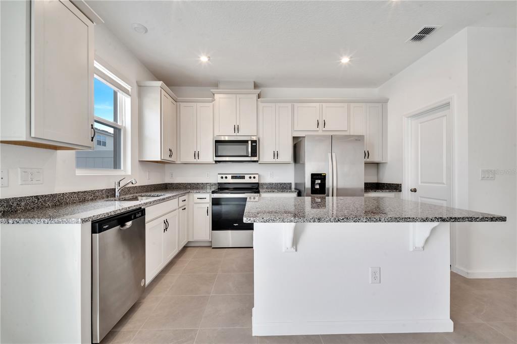 9068 Ocean Tide Way Kissimmee, FL 34747 - Photo 10 of 42 a kitchen with kitchen island granite countertop a stove a sink a refrigerator and white cabinets