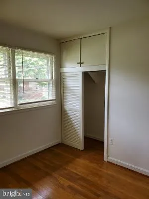 an empty room with wooden floor closet and windows
