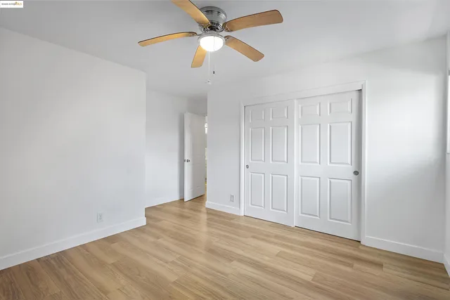 an empty room with wooden floor closet and fan
