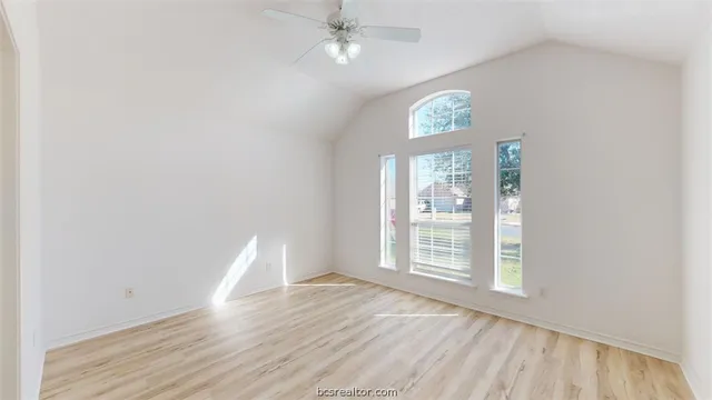 an empty room with wooden floor chandelier fan and windows