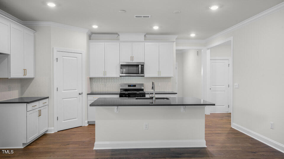 2222 Redpoll Drive Apex, NC 27539 - Photo 8 of 38 a kitchen with kitchen island white cabinets and stainless steel appliances