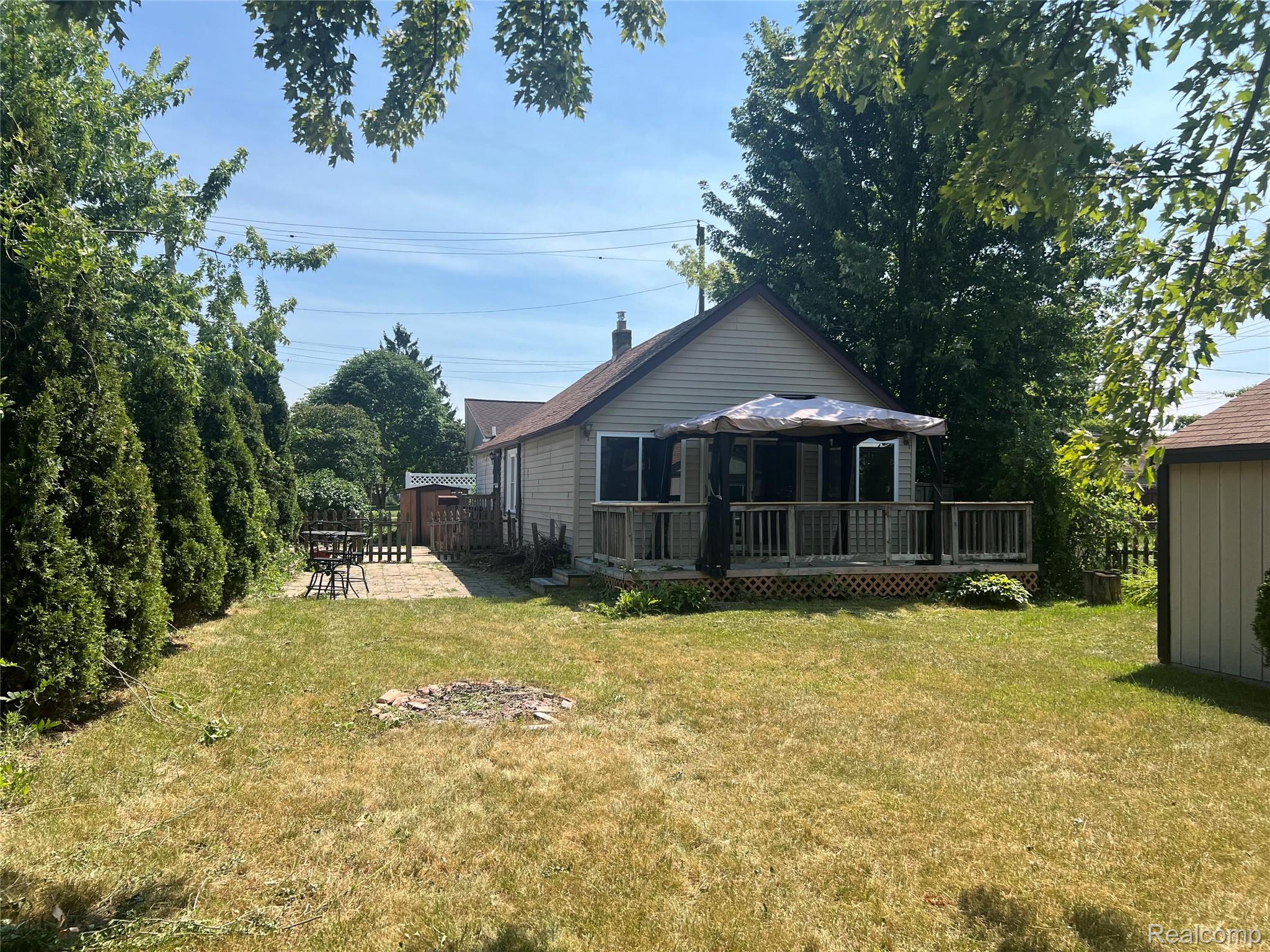 15676 Frazho Road Roseville, MI 48066 - Photo 20 of 20 Expansive backyard featuring a large grass area, a dedicated patio space with pavers, a raised wood deck, and mature privacy trees
