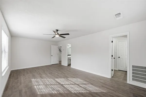 an empty room with wooden floor ceiling fan and windows