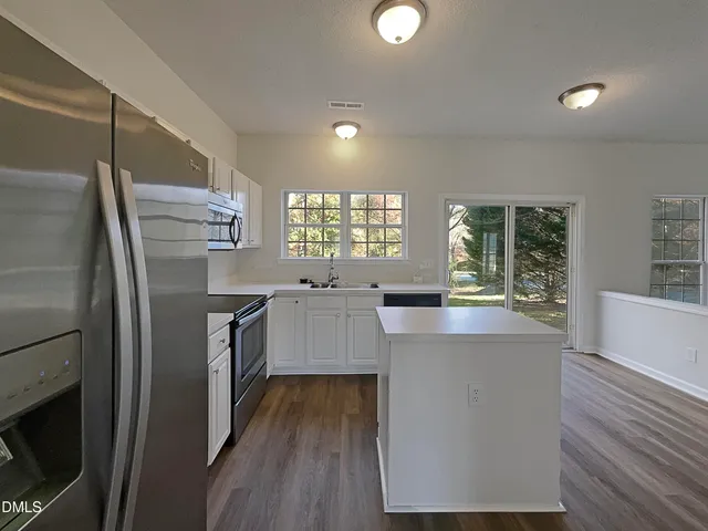 a kitchen with stainless steel appliances a refrigerator a sink a stove and white cabinets with wooden floor