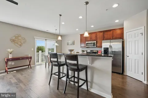 a kitchen with stainless steel appliances granite countertop a stove a refrigerator a kitchen island a dining table and chairs with wooden floor