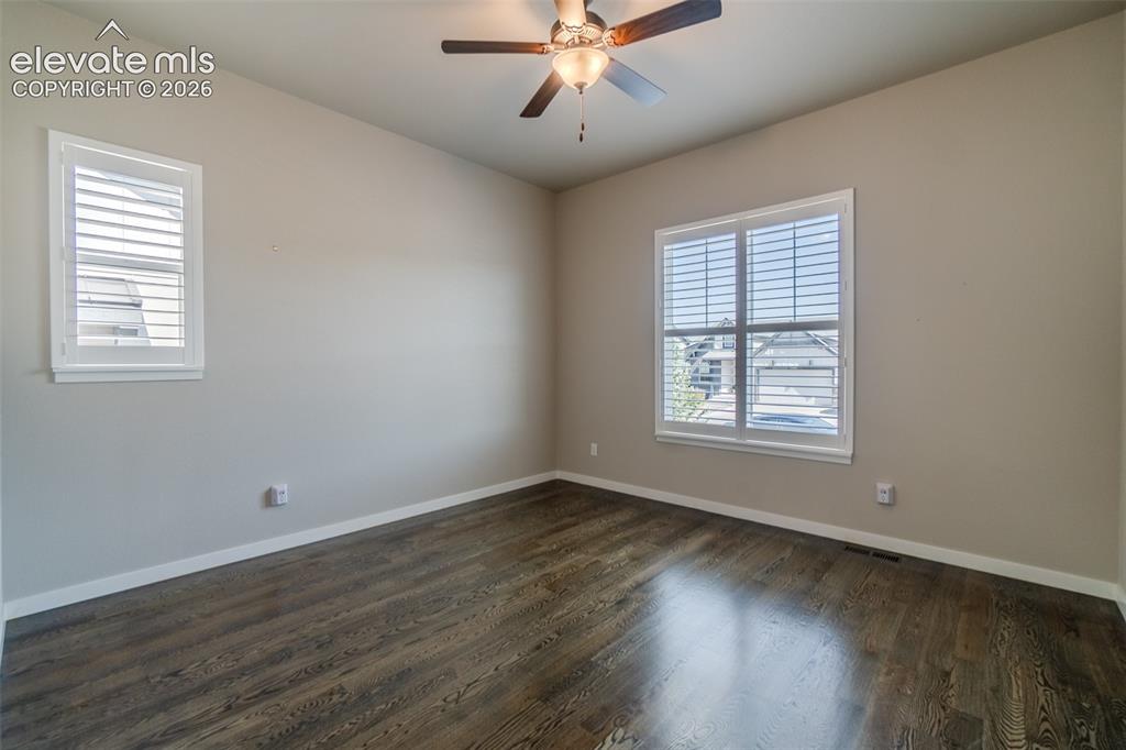 1061 Native Dancer Terrace Colorado Springs, CO 80921 - Photo 19 of 50 Spacious room featuring wood-finish flooring, two windows with white louvered shutters, a ceiling fan with integrated lighting, and neutral wall paint
