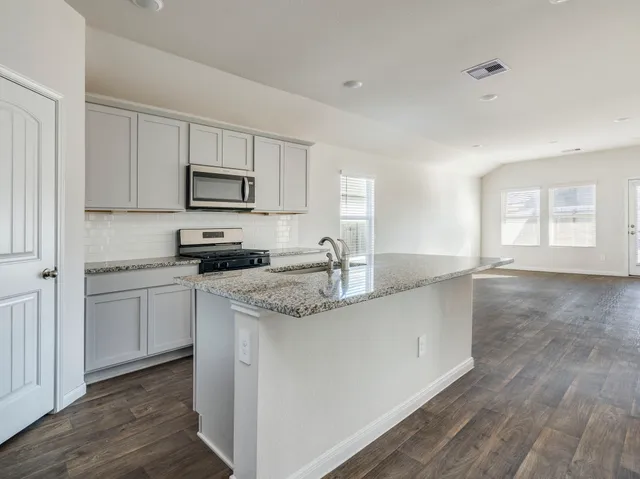 a kitchen with stainless steel appliances granite countertop a sink a stove a refrigerator with white cabinets and wooden floor