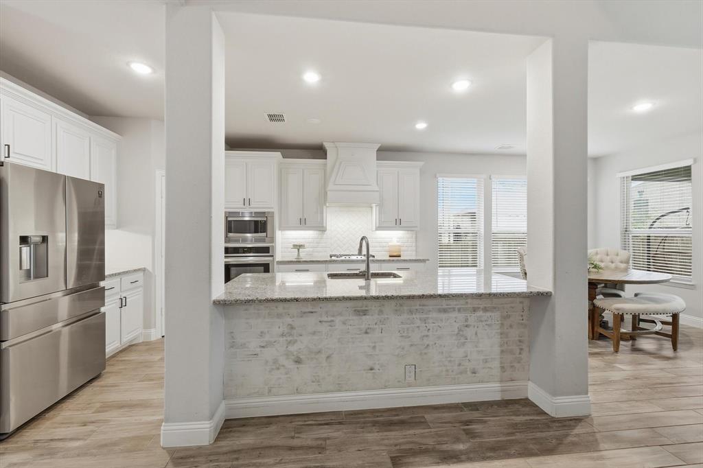 924 Timber Ridge Drive Justin, TX 76247 - Photo 9 of 32 Kitchen featuring a large island with a stone countertop and brick-patterned facade, white cabinetry, stainless steel appliances, wood-finish flooring, and recessed lighting