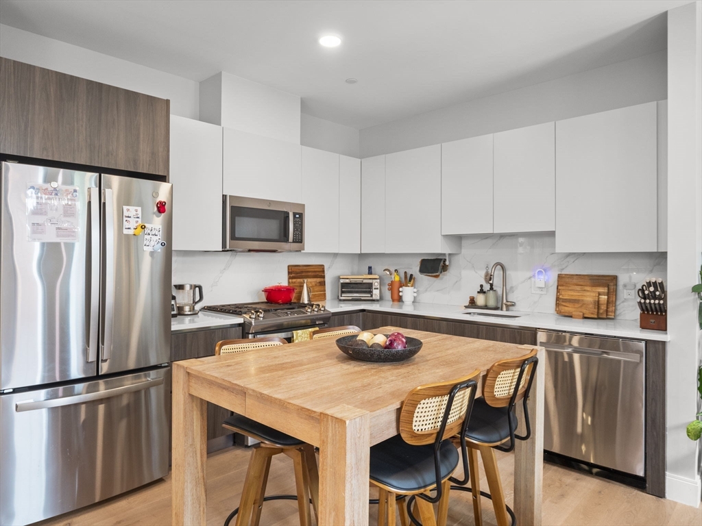 a kitchen with stainless steel appliances a stove a sink dishwasher a refrigerator with a dining table and chairs