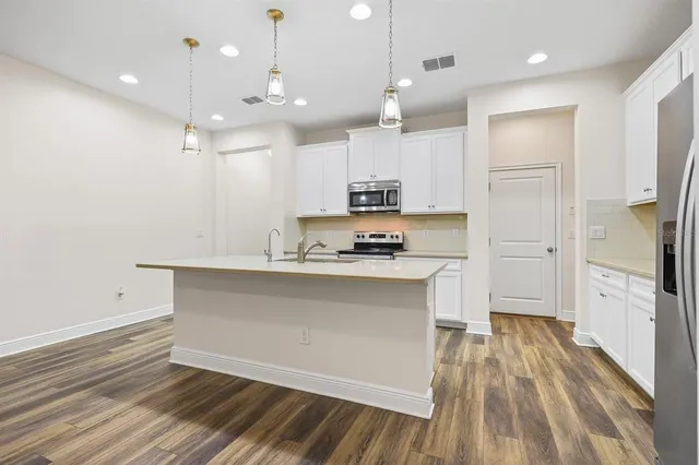 a large kitchen with cabinets a sink dishwasher a refrigerator and a stove with wooden floor