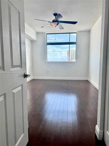an empty room with wooden floor chandelier fan and windows