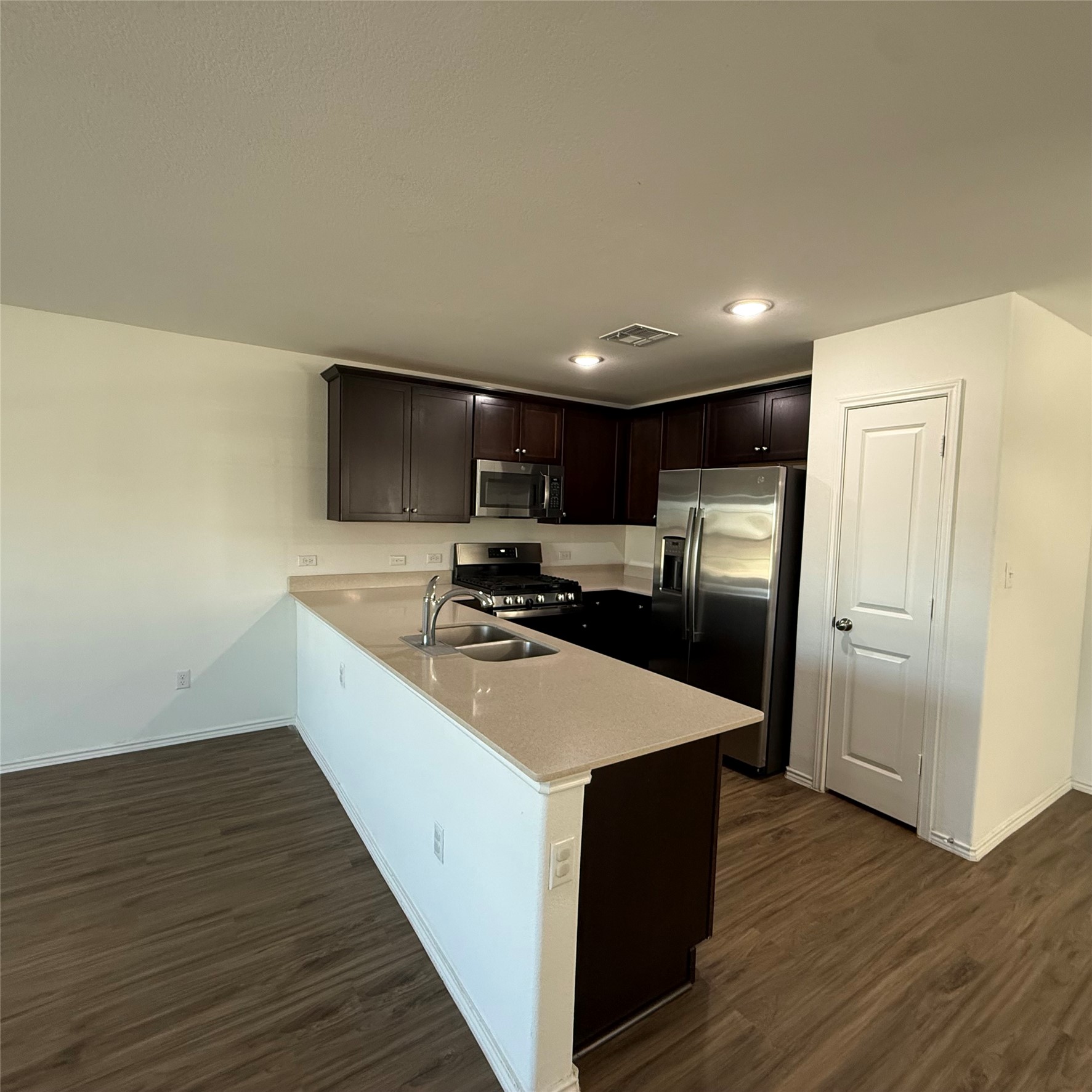 13711 Mussel Run Elgin, TX 78621 - Photo 16 of 31 Kitchen with a peninsula, dark wood finish cabinetry, stainless steel appliances, dark wood-style flooring, and light stone countertops