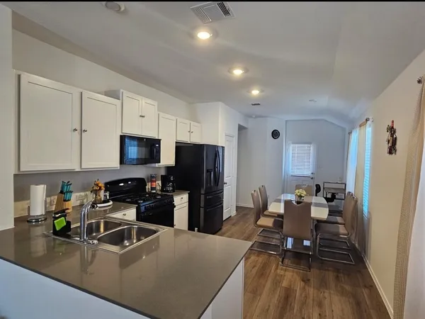 a kitchen with stainless steel appliances a stove a sink a refrigerator white cabinets and wooden floor