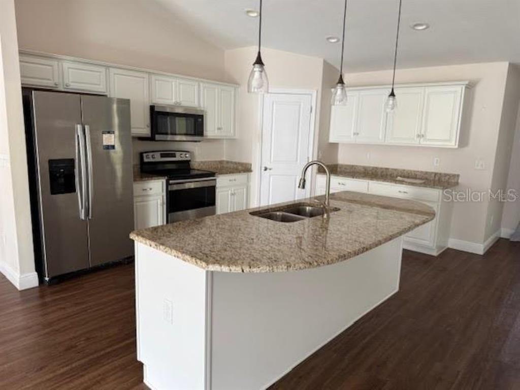 3707 Southeast 24th Street Ocala, FL 34471 - Photo 3 of 14 a kitchen with stainless steel appliances granite countertop a sink a microwave a refrigerator and white cabinets with wooden floors