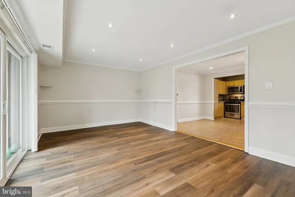 a view of empty room with wooden floor and kitchen