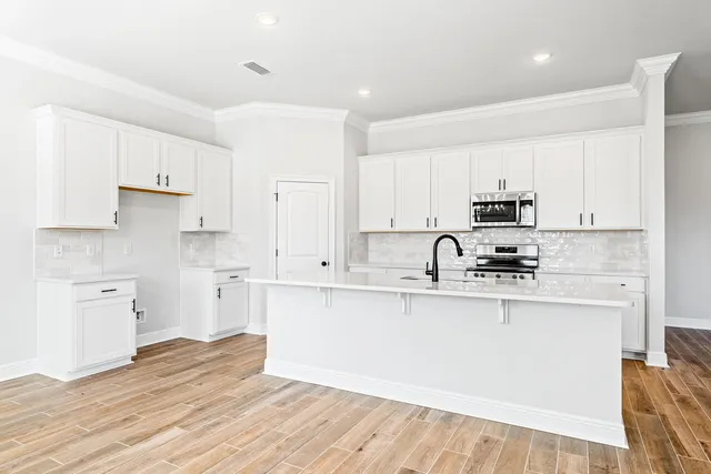 a kitchen with stainless steel appliances granite countertop a sink a stove a refrigerator and white cabinets with wooden floor