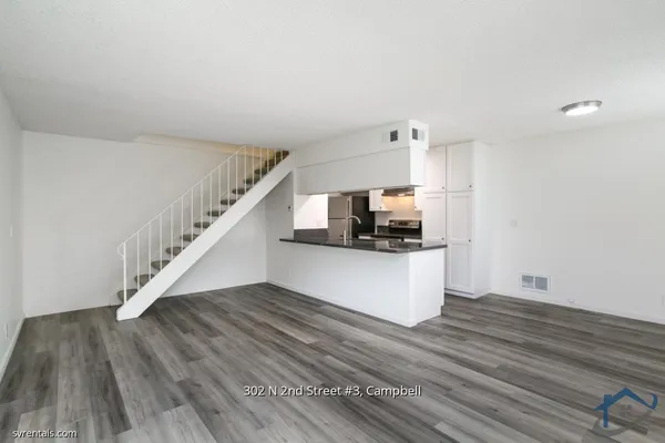 a view of kitchen and empty room with wooden floor
