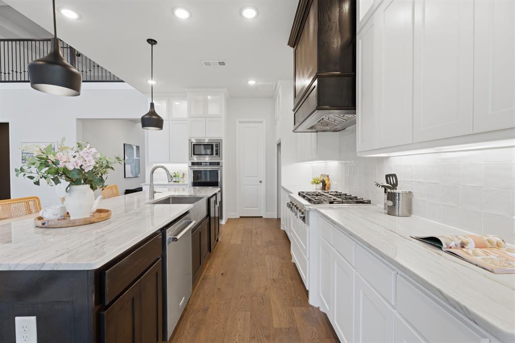 1316 Limestone Ridge Road Mansfield, TX 76063 - Photo 12 of 40 Gourmet kitchen featuring a large island, stainless steel appliances, white cabinetry, wood-finish flooring, and pendant lighting